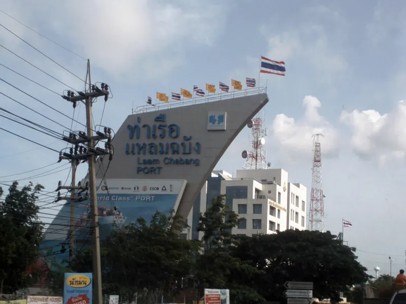 The Laem Chabang Port entrance sign with Thai and English lettering, flags and power lines against a cloudy sky.