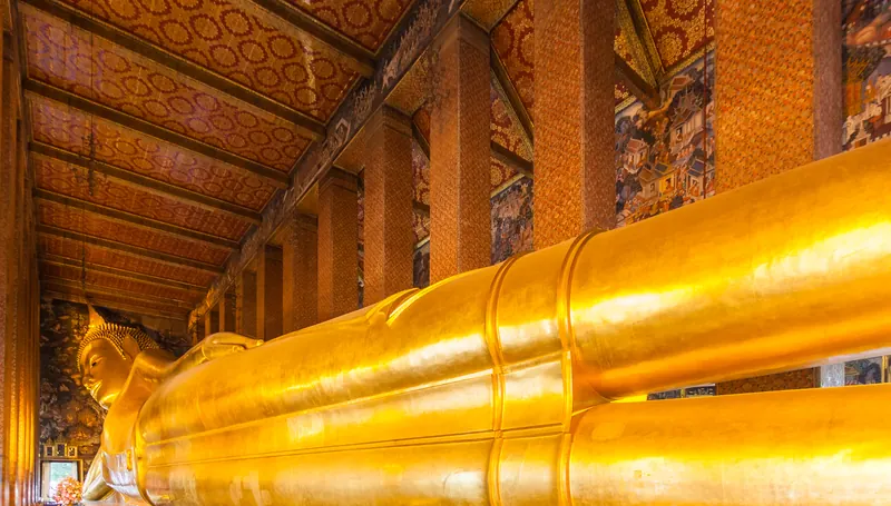 The gold-plated Reclining Buddha at Wat Pho, stretching along a hall with ornate red and gold pillars.